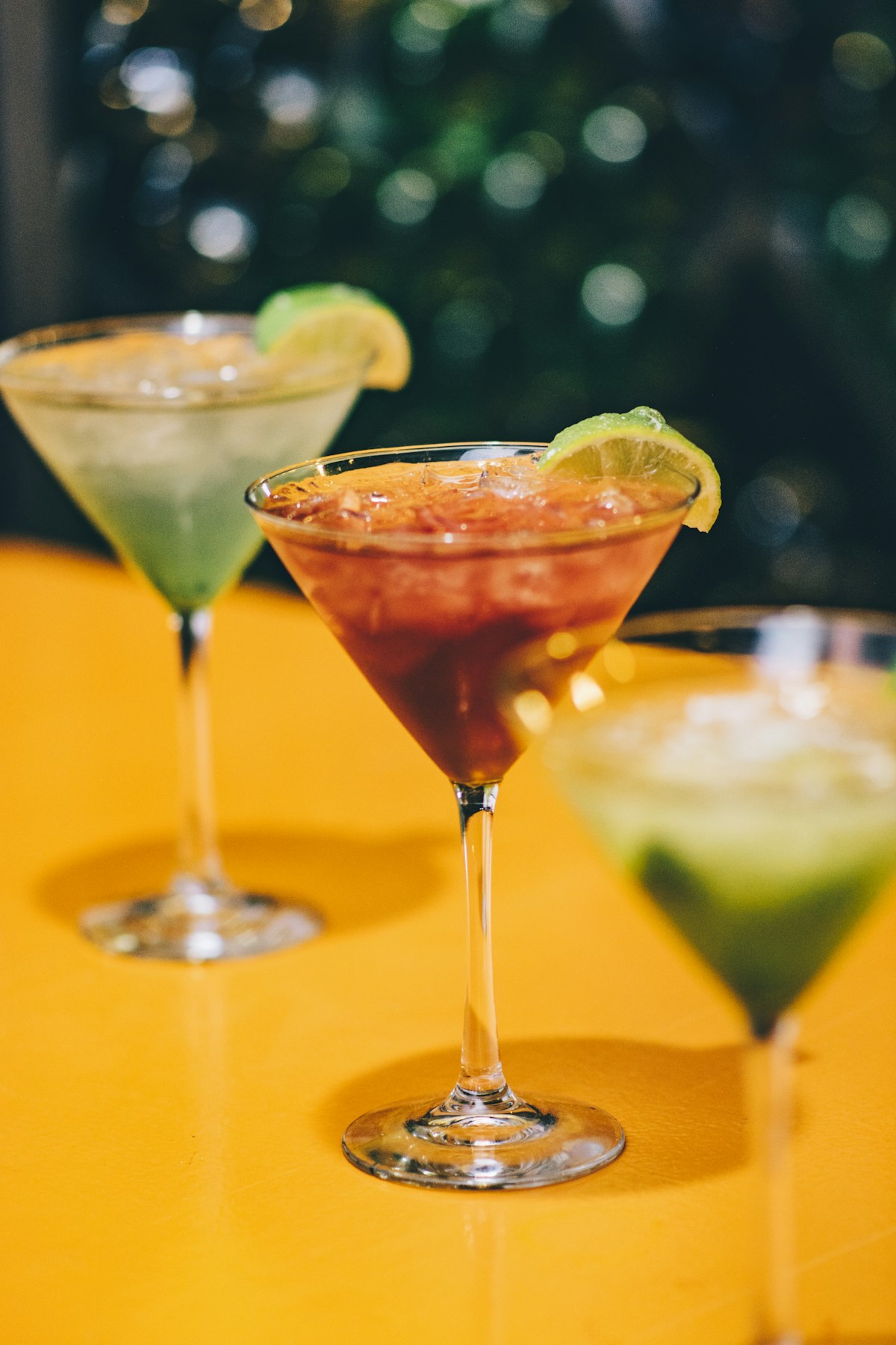 Vibrant colorful fruit drinks with lime garnish on a sunny yellow table