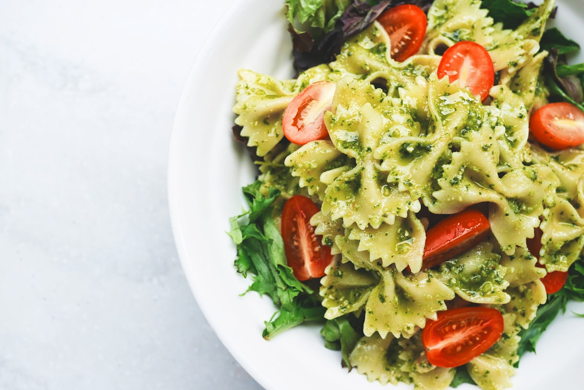 Creamy pasta salad with fresh greens and cherry tomatoes in a white bowl