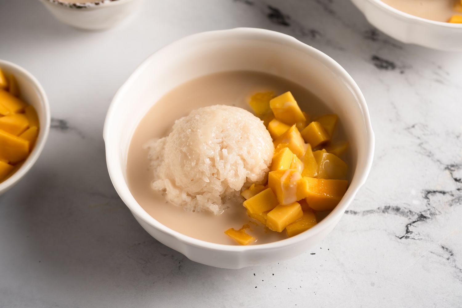 Mango sticky rice with coconut sauce being poured over ripe mango slices and glutinous rice