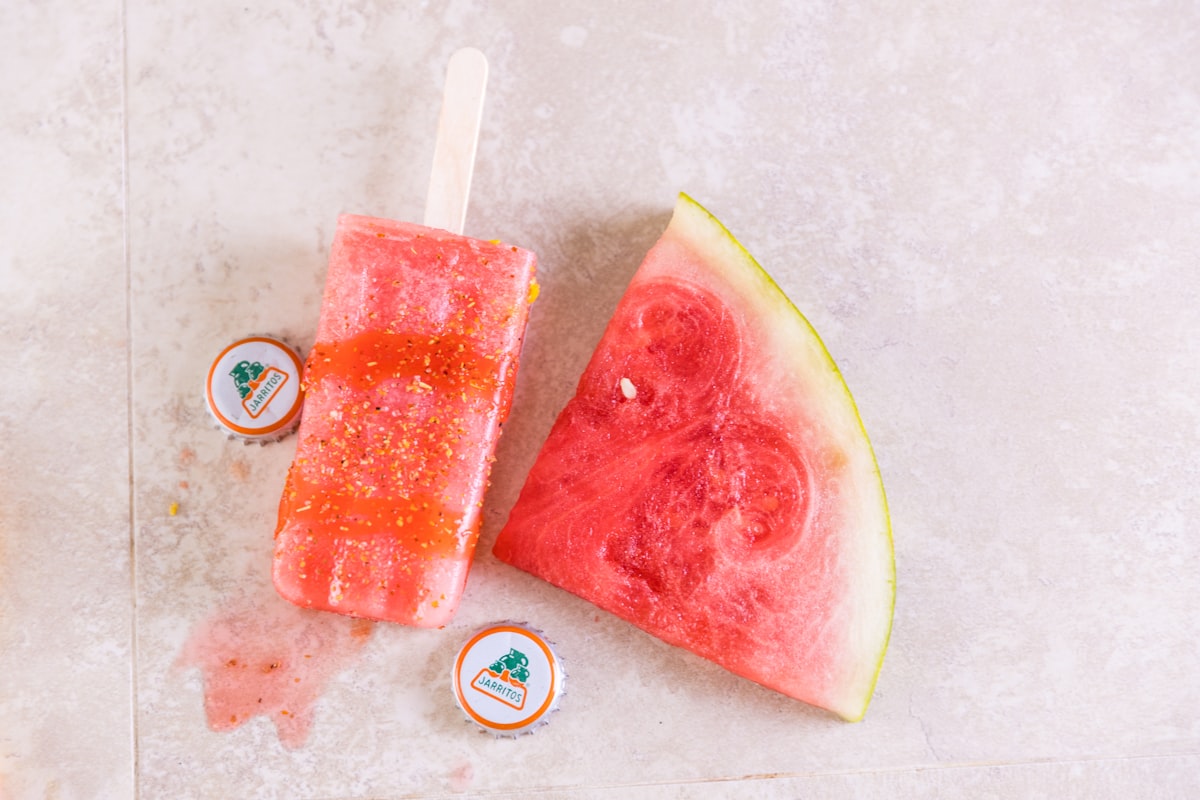 Watermelon frozen dessert next to a fresh slice of watermelon on a light stone surface