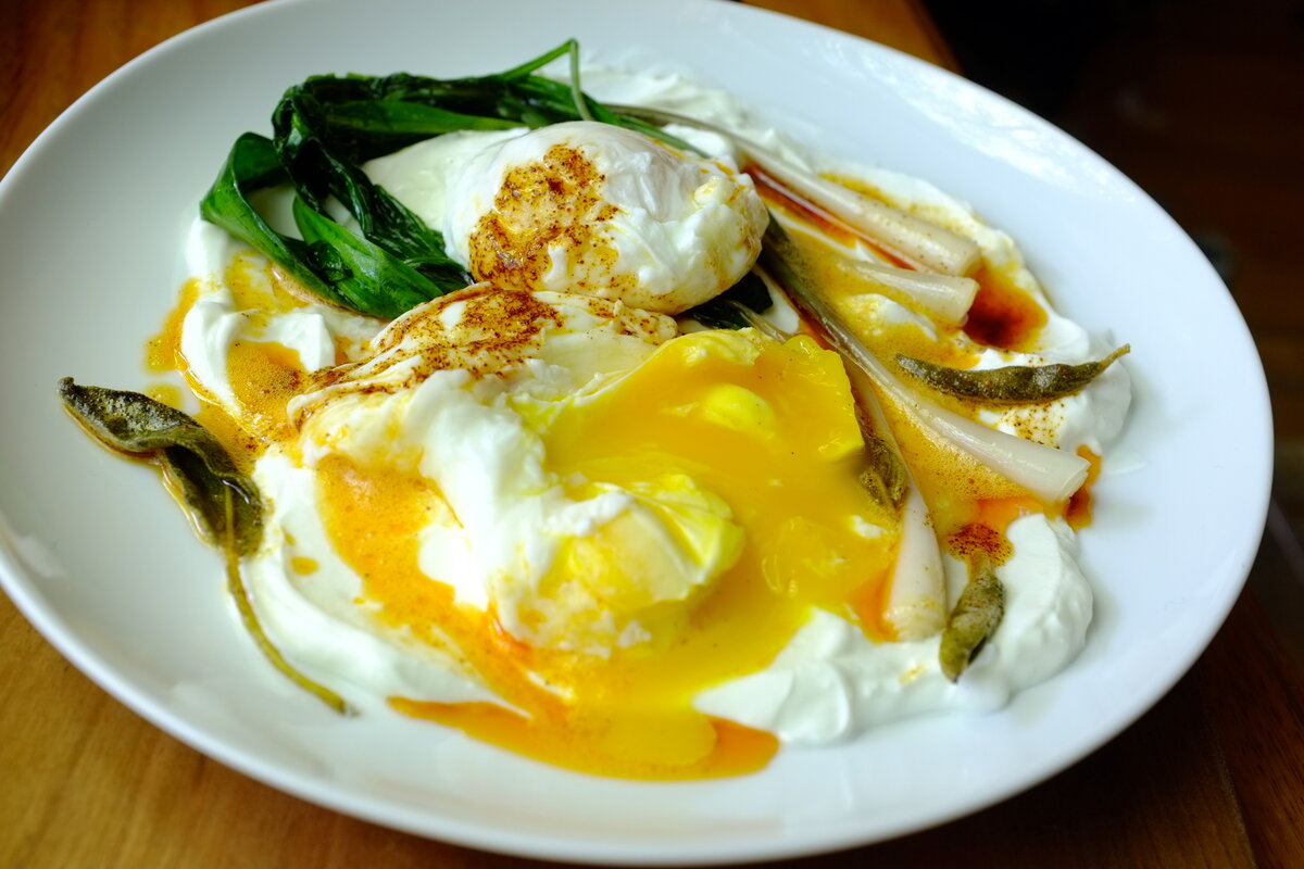Turkish eggs Çılbır — poached eggs over garlicky yogurt with spiced red butter sauce and fresh herbs